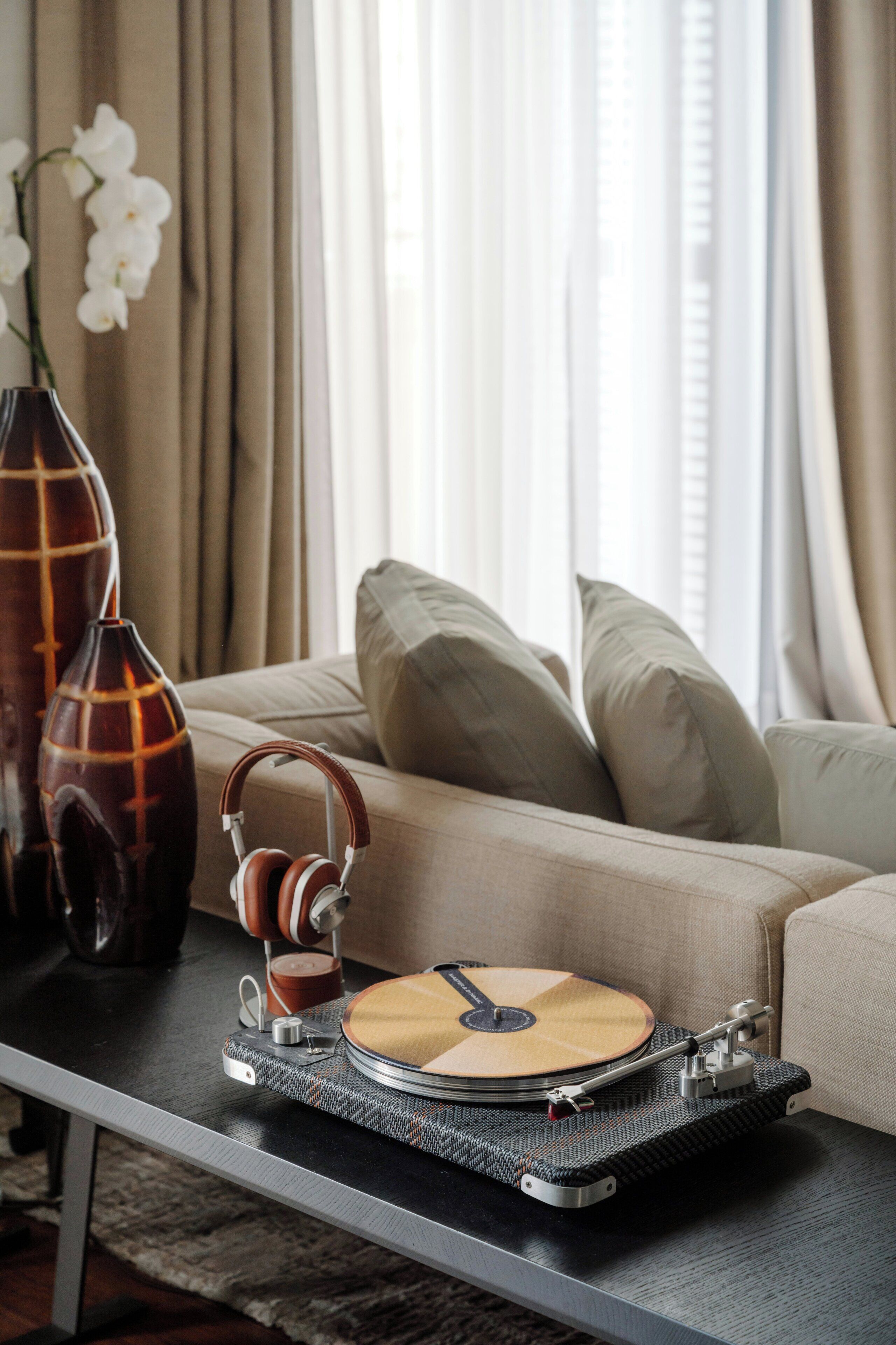 A turntable on a table, a vase, and a sofa with cushions.