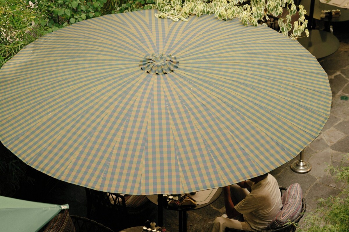 An outdoor seating area with checkered umbrellas, wicker chairs, and a stone floor.