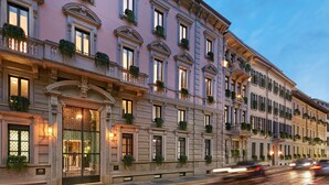 Un edificio de varios pisos con detalles arquitectónicos ornamentales, incluyendo columnas, balcones con vegetación y una entrada bien iluminada.