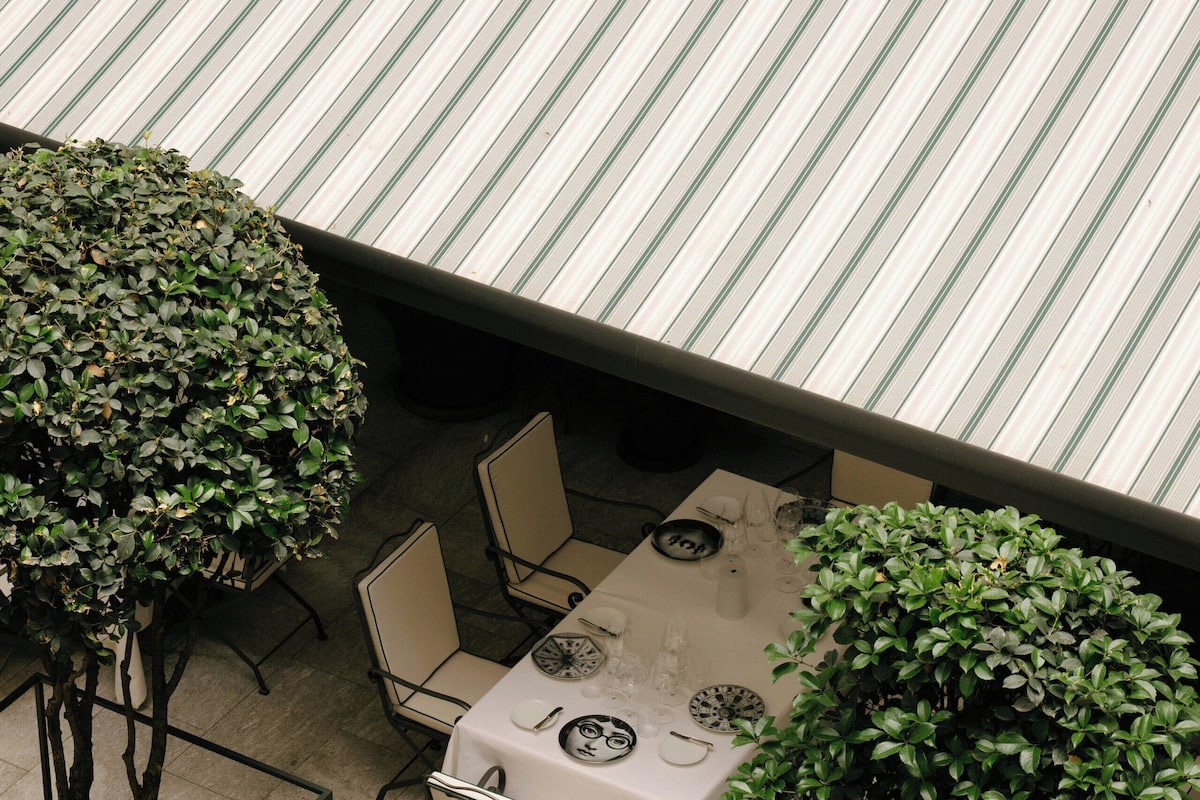 An outdoor dining area with a table set for two, surrounded by chairs, and enclosed by a metal railing.