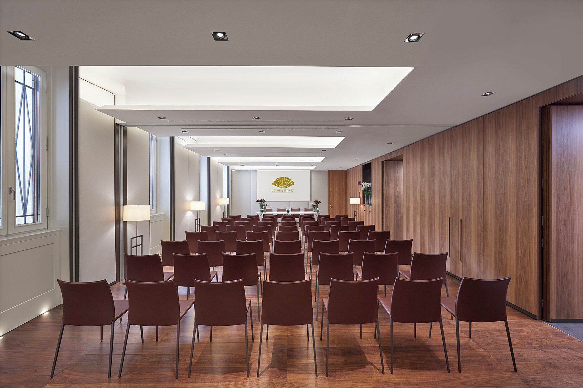 Een vergaderzaal met rijen stoelen, een lange tafel en een groot raam.