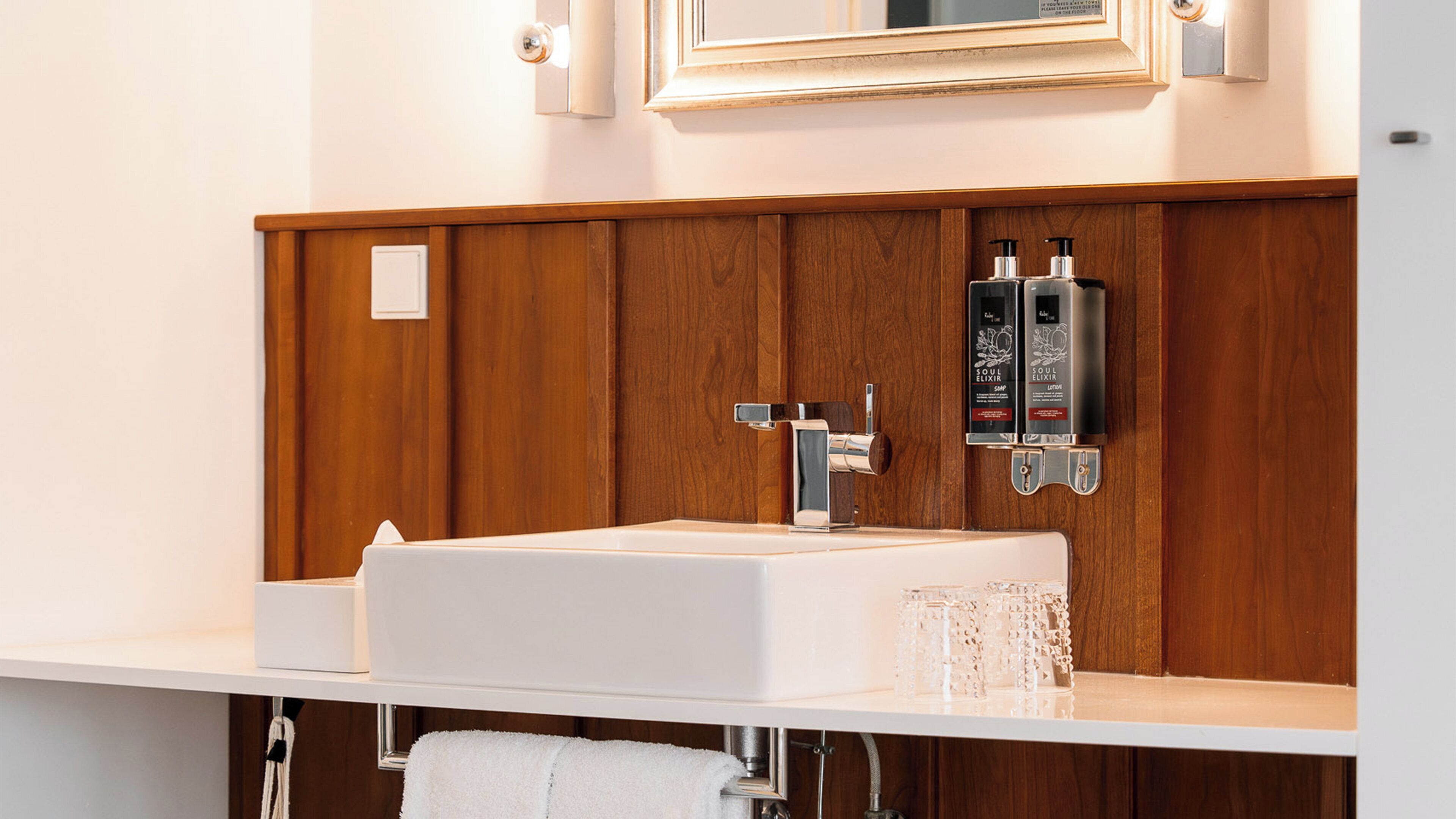 A bathroom with a white sink, wooden paneling, a mirror, and two soap dispensers.