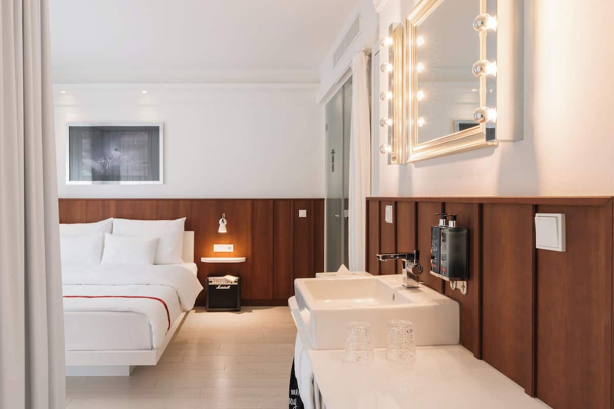 A hotel room with a bed, bedside lamp, vanity with mirror, and a framed picture on the wall.