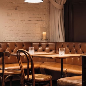 A corner booth with a cushioned bench, a wooden table, and two chairs. A candle is on a small table in the background. - Ruby Sofie Hotel Vienna by IHG (Vienna)