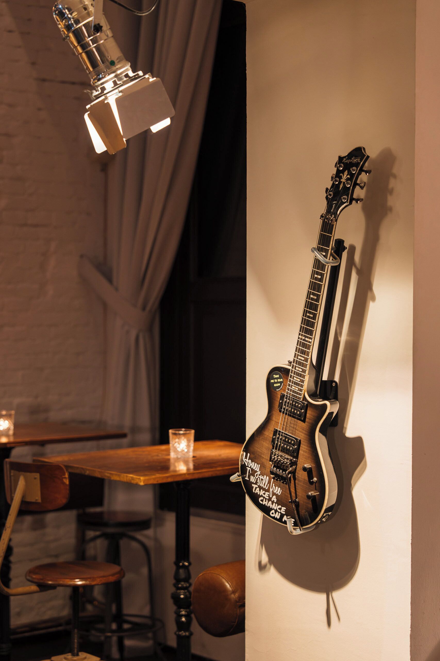 En guitar hængt på væggen, et bord med en stol og en lampe.