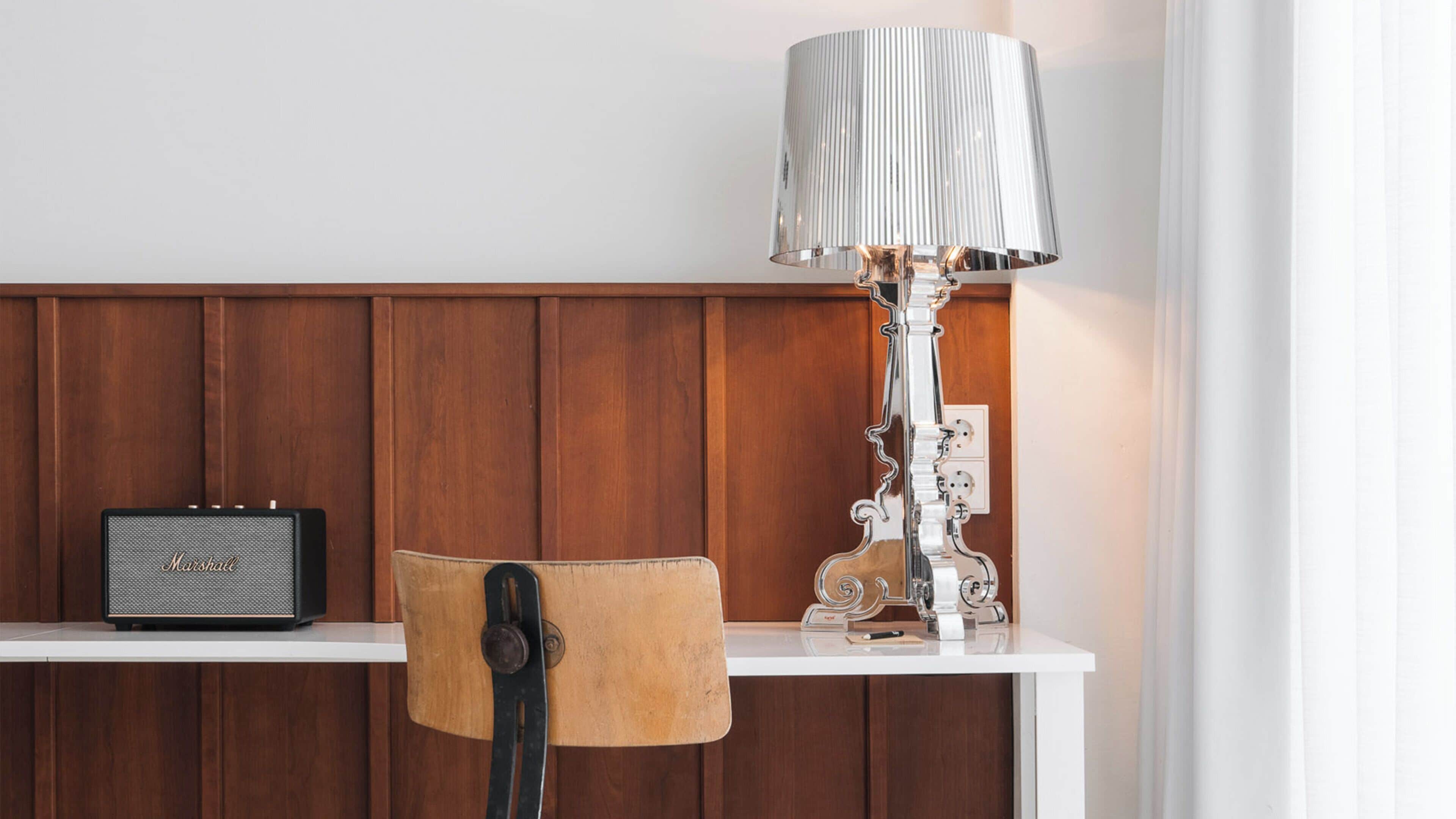 A wooden panel wall, a white table with a lamp and a radio, and a chair with a wooden backrest.