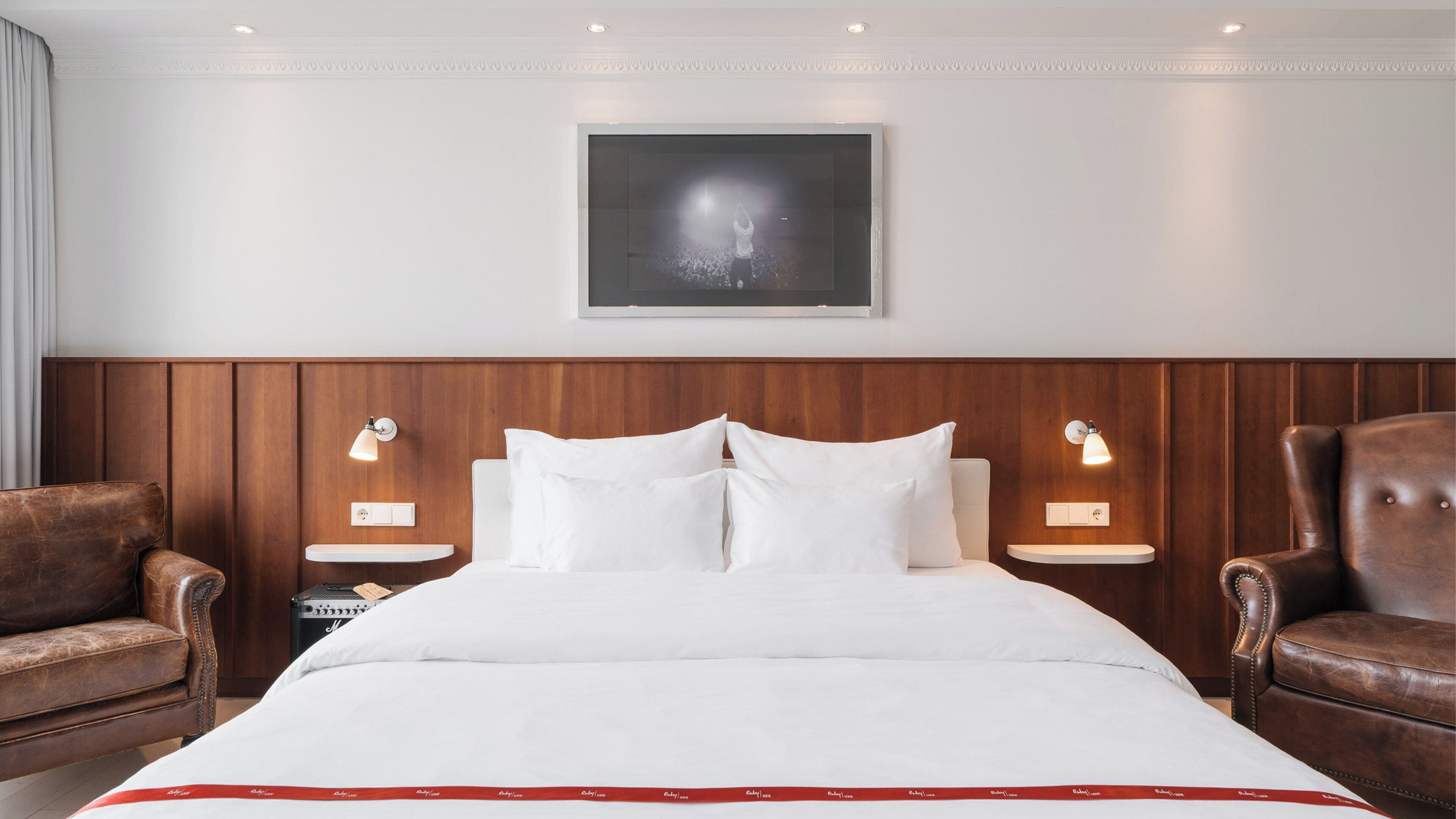 A hotel room with a large bed, two nightstands, a wooden headboard, and two leather armchairs.