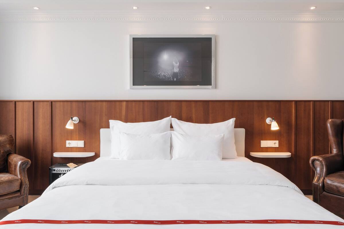 A hotel room with a large bed, two nightstands, a wooden headboard, and two leather armchairs.