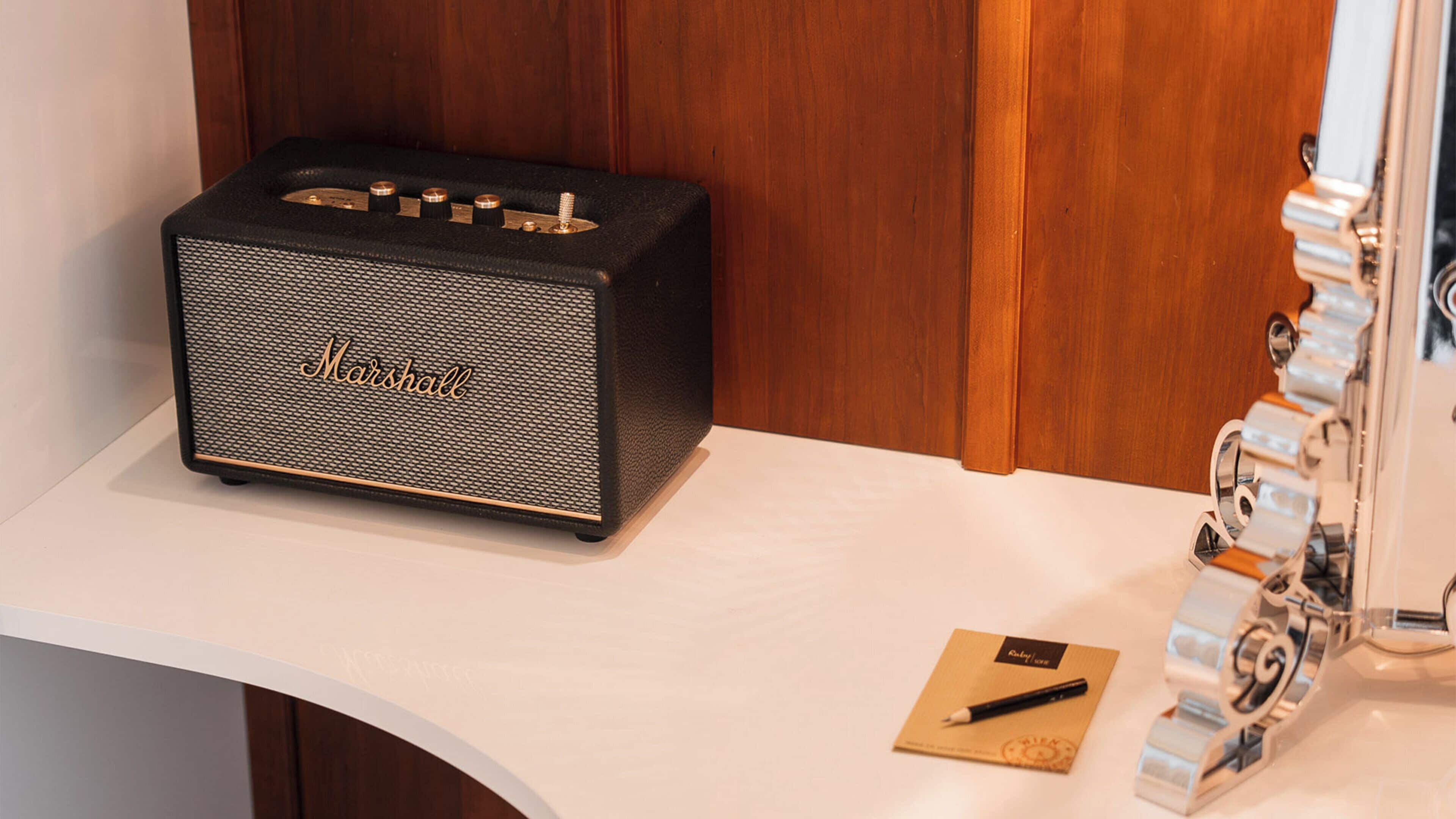 A Marshall amplifier on a white surface with a wooden panel in the background.