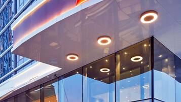 Fachada moderna de hotel con ventanales de vidrio, un llamativo letrero de 'ibis Hotels' y luminarias circulares.