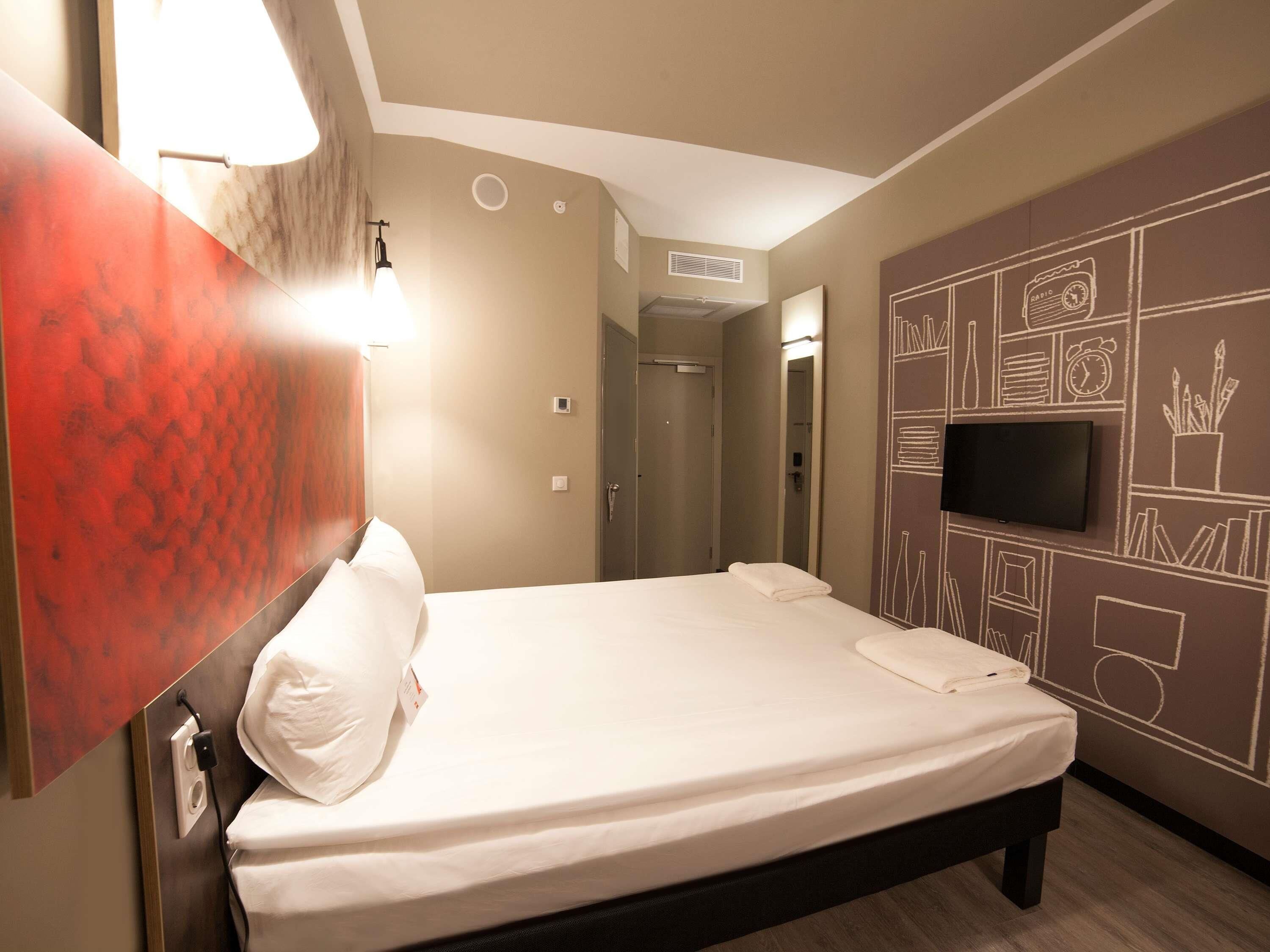 A hotel room with a bed, a television, and a wall with a chalkboard design.