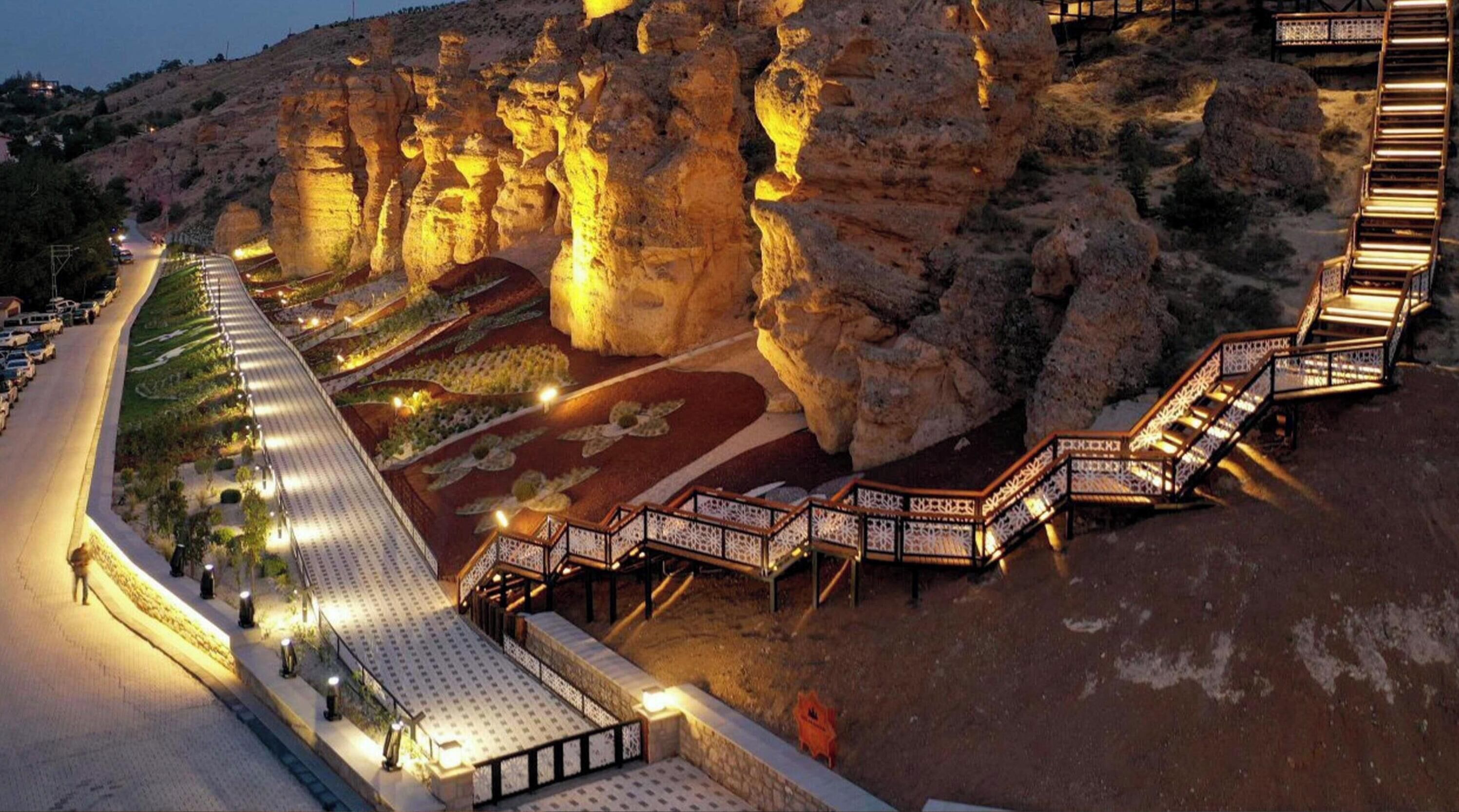 A well-lit outdoor area with a pathway leading to a staircase, surrounded by rock formations.