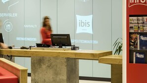 A hotel reception desk with a computer, a clock, and a red information stand. - Ibis Konya (Konya)
