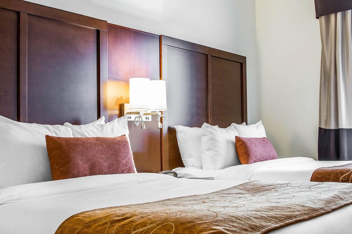 Une chambre d’hôtel avec un grand lit, une tête de lit en bois, une table de chevet avec une lampe et une fenêtre avec des rideaux.