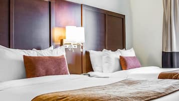 Habitació d'hotel amb un llit gran, un reposacapses de fusta, una taula de nit amb una làmpada i una finestra amb cortines.