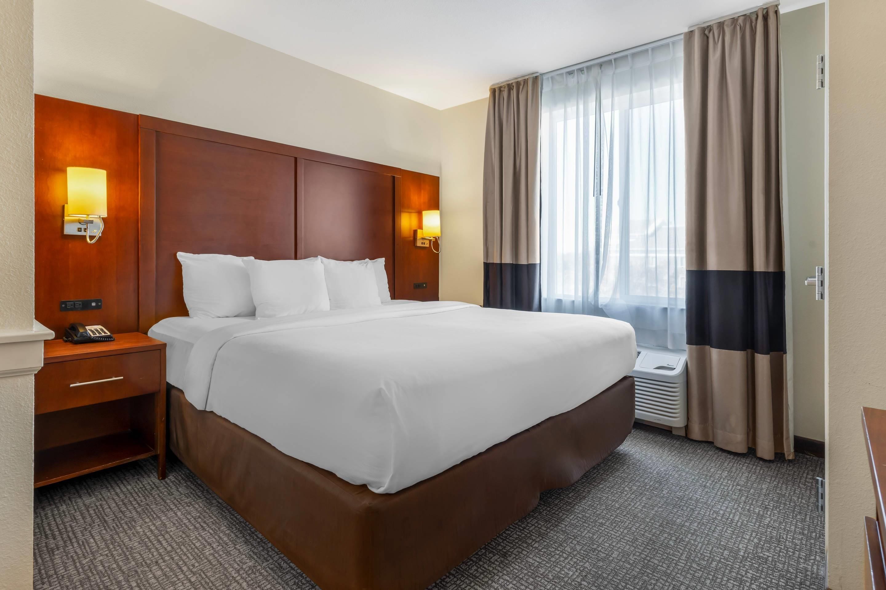 A hotel room with a large bed, bedside lamps, a telephone, and a window with curtains.