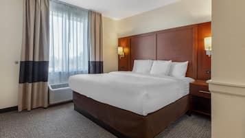 A hotel room with a large bed, a bedside table, a lamp, and a window with curtains.