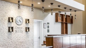 A reception area with a stone wall, a wooden reception desk, and multiple pendant lights. - Comfort Suites Woodland - Sacramento Airport (Woodland)