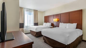 A hotel room with two beds, a desk, a TV, and an air conditioning unit.