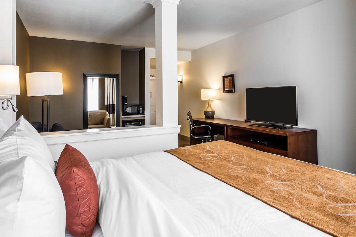Une chambre d’hôtel équipée d’un lit, d’un bureau, d’une télévision, d’un miroir et d’une machine à café.
