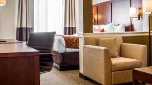 A hotel room with a bed, a desk, a chair, a sofa, and a large mirror. - Comfort Suites Woodland - Sacramento Airport (Woodland)
