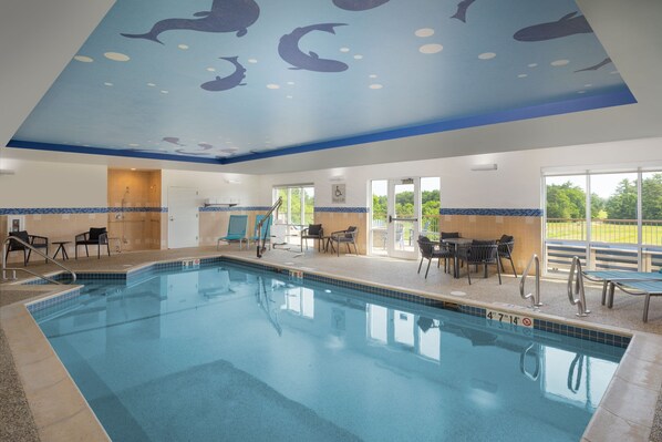 An indoor swimming pool with a ceiling mural of dolphins, a sunroof, and a patio area with chairs and tables.