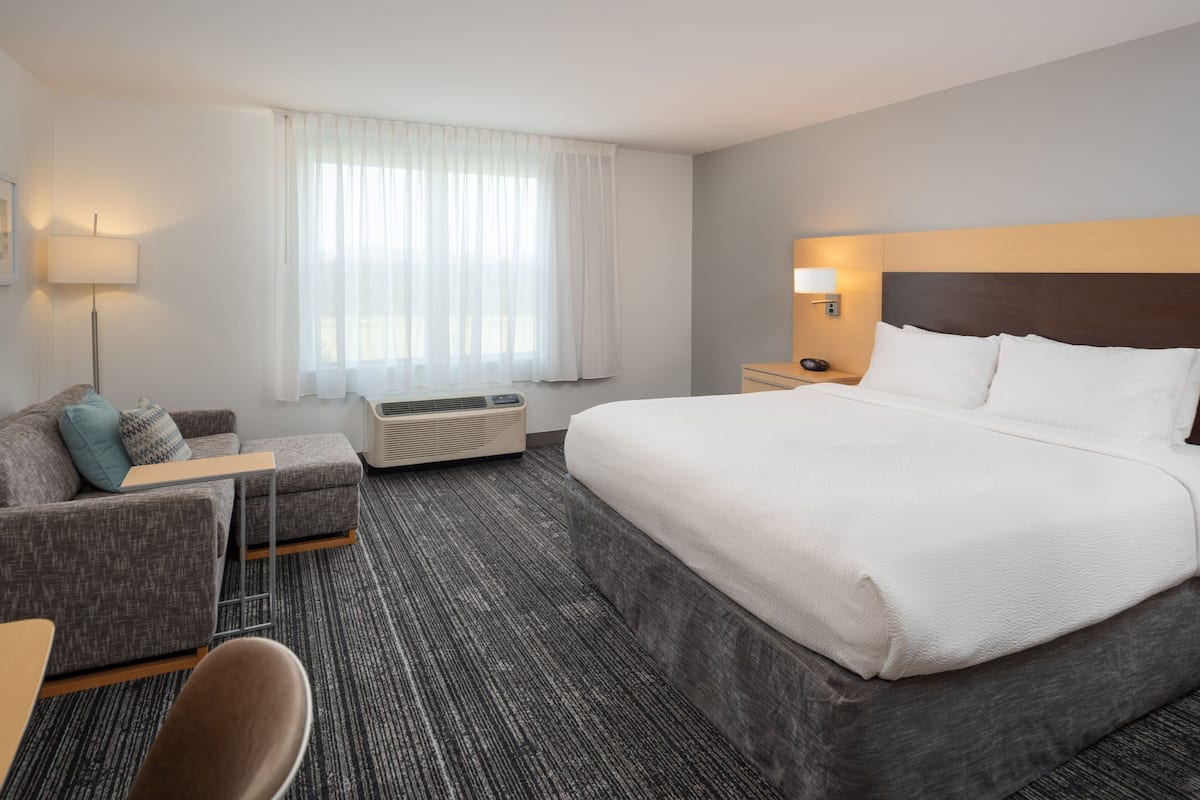 Une chambre d’hôtel avec un grand lit, un canapé, un bureau et une fenêtre avec des rideaux.