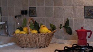 Una cucina con un cesto di vimini contenente limoni e una caffettiera rossa sul fornello.
