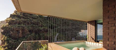 A wooden hot tub with two towels on a balcony overlooking a mountainous landscape.