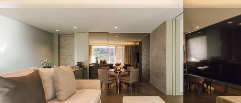 A modern living room with a sofa, ottoman, and a dining area with a table and chairs.