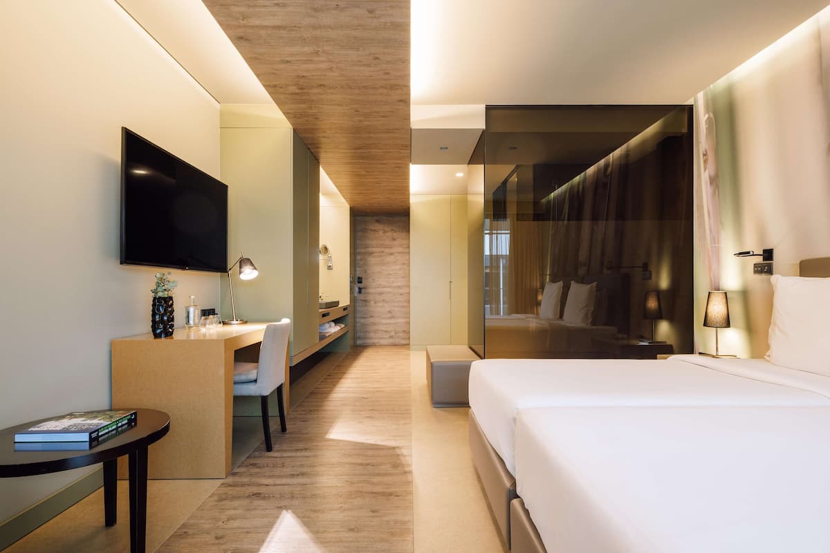 A modern hotel room with a flat-screen TV, a desk with a chair, a bed, and a large mirror.