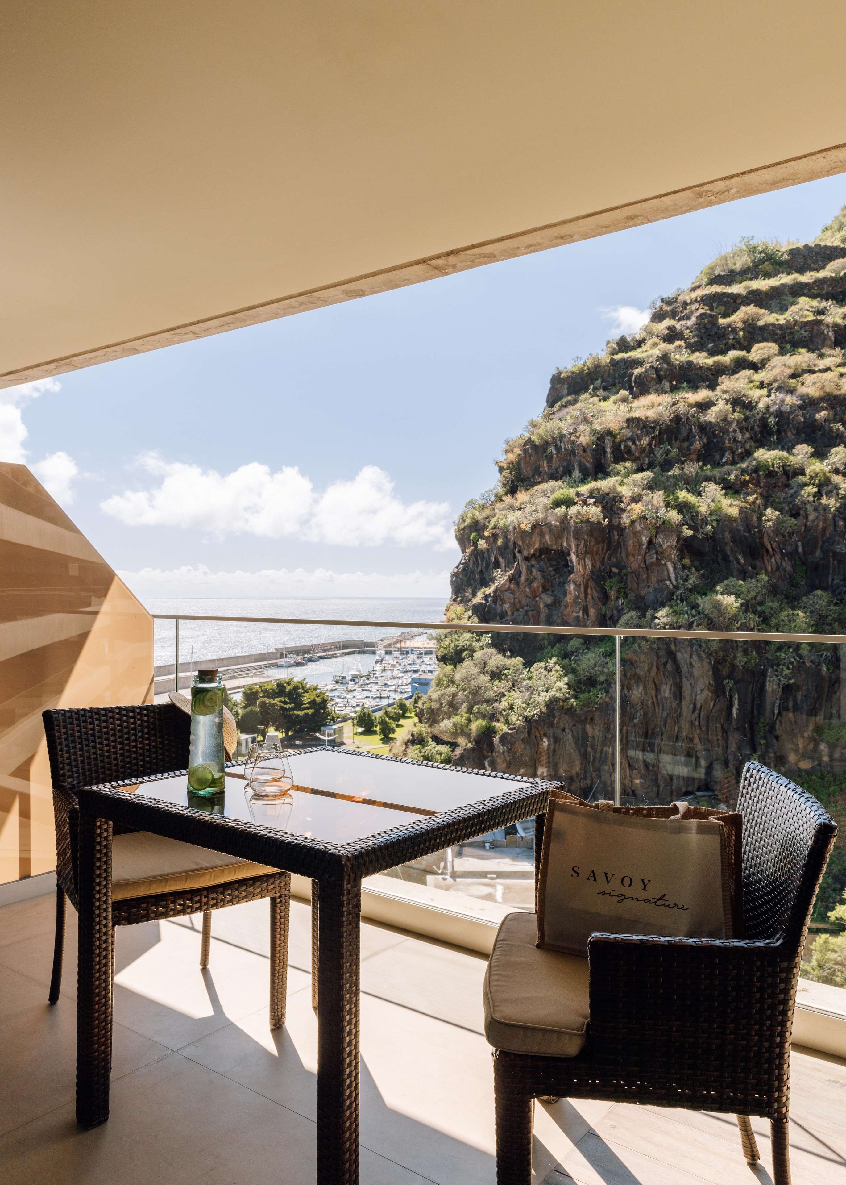 Un balcon agrémenté de meubles en osier, d’une table en verre et offrant une vue sur une ville côtière et des falaises.