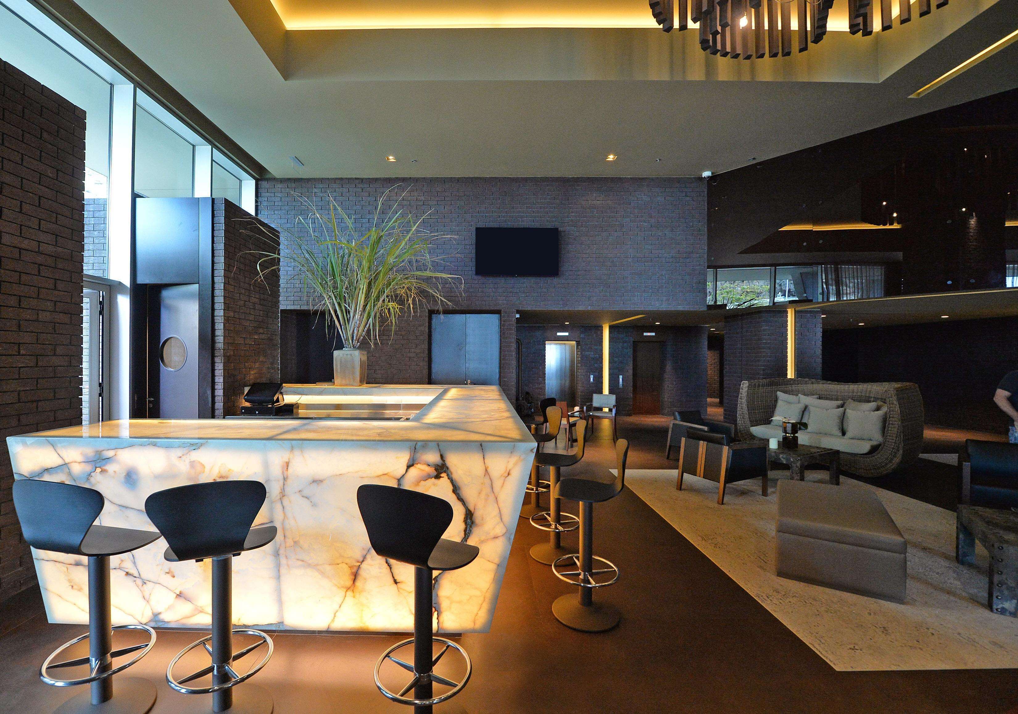 A modern bar area with a marble countertop, black bar stools, and a large potted plant.
