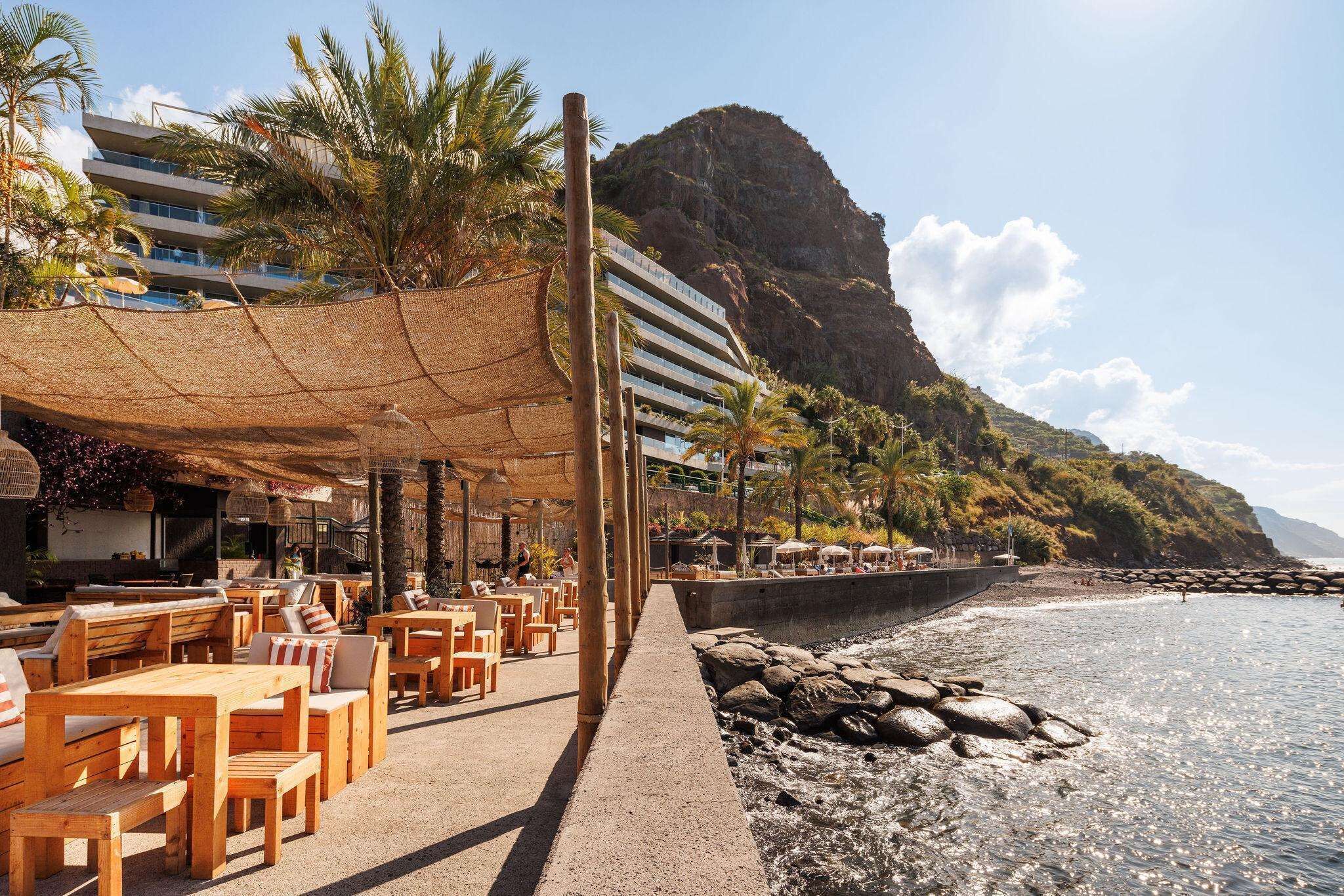 Un restaurant situé en bord de mer, avec une terrasse, une vue sur l’océan et une montagne en arrière-plan.