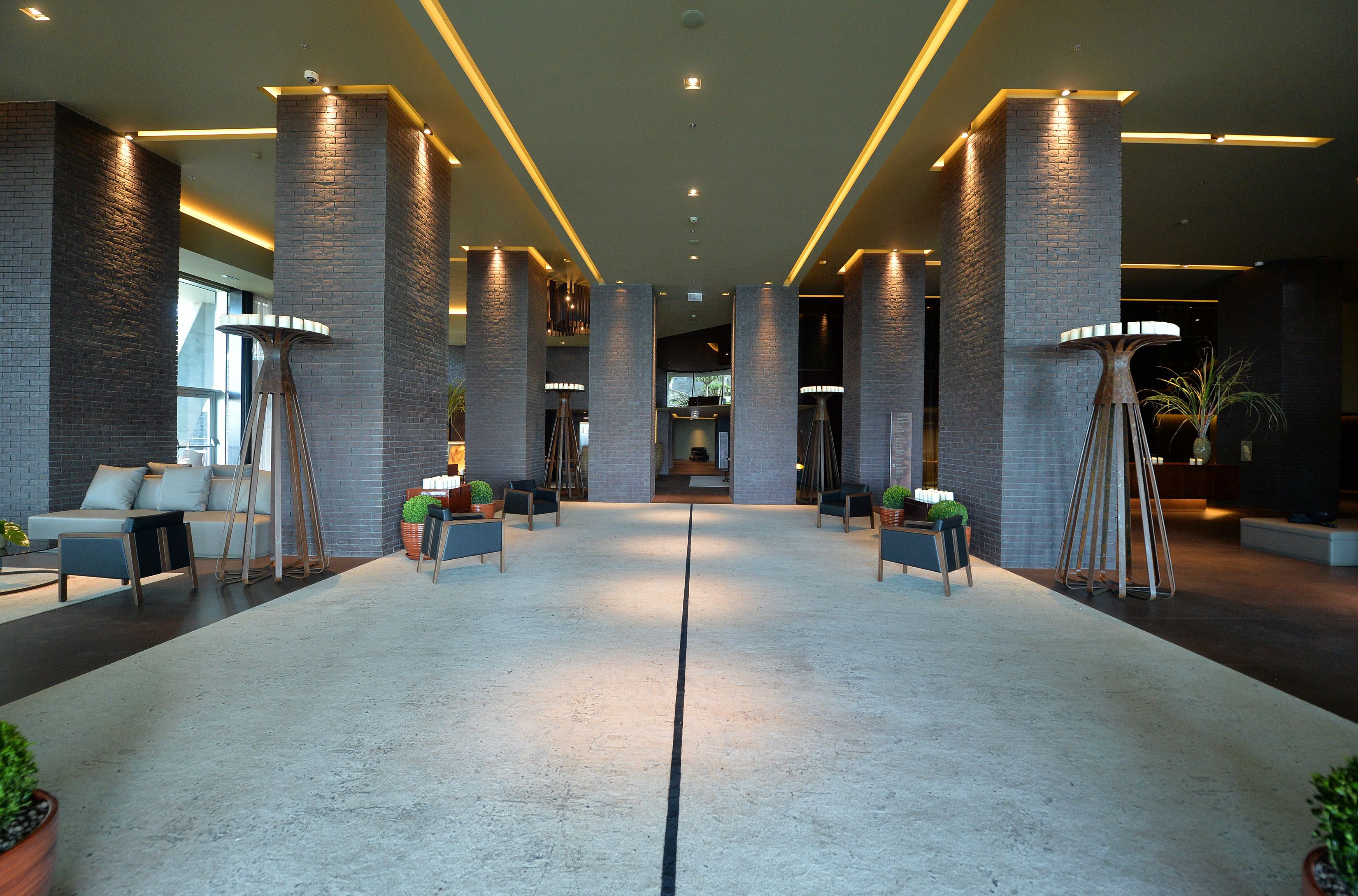 Een ruime lobby met hoge plafonds, bakstenen zuilen en moderne verlichtingsarmaturen.