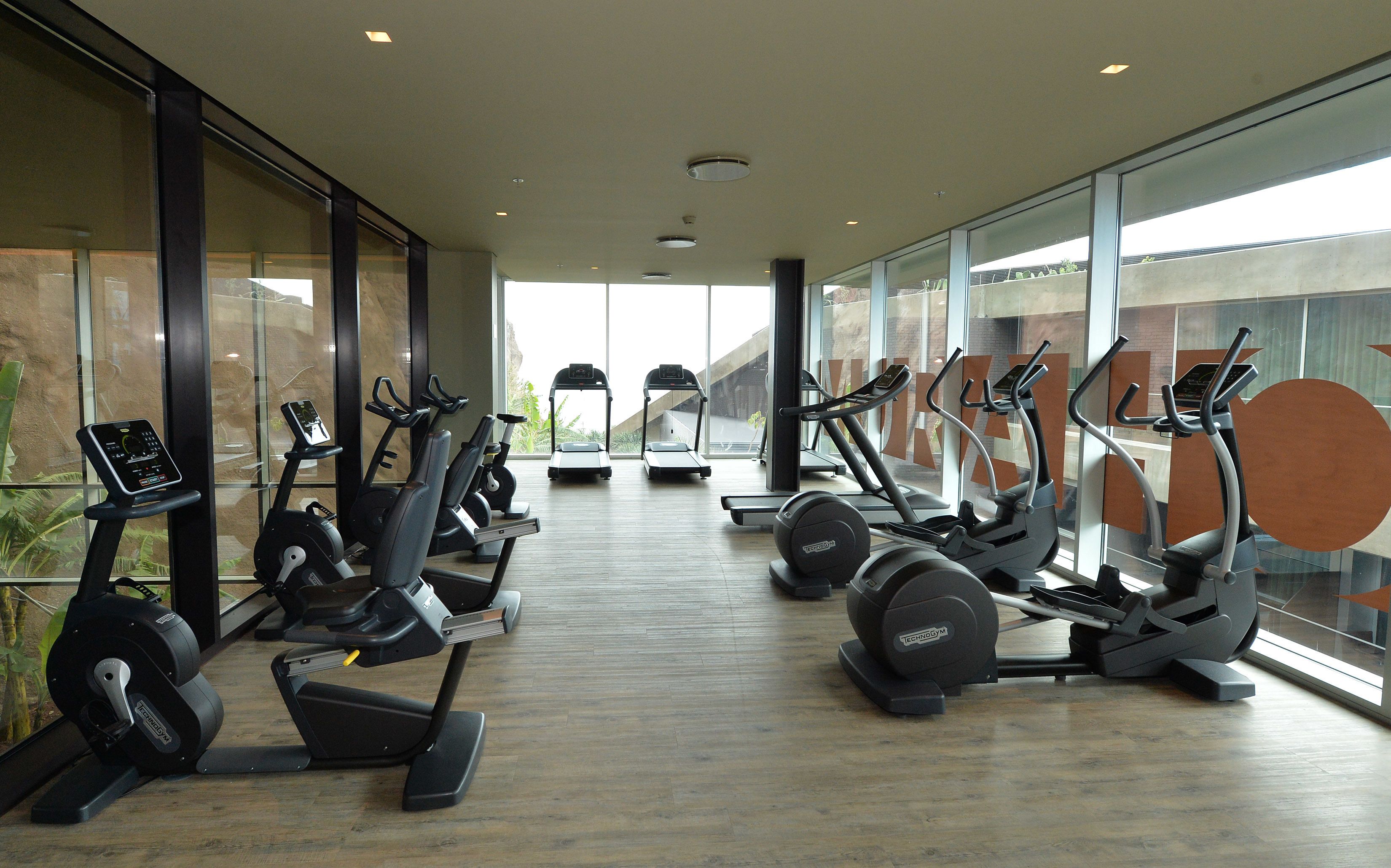 Une salle de sport équipée de divers appareils de cardio, dotée de grandes fenêtres et présentant un aménagement intérieur moderne.