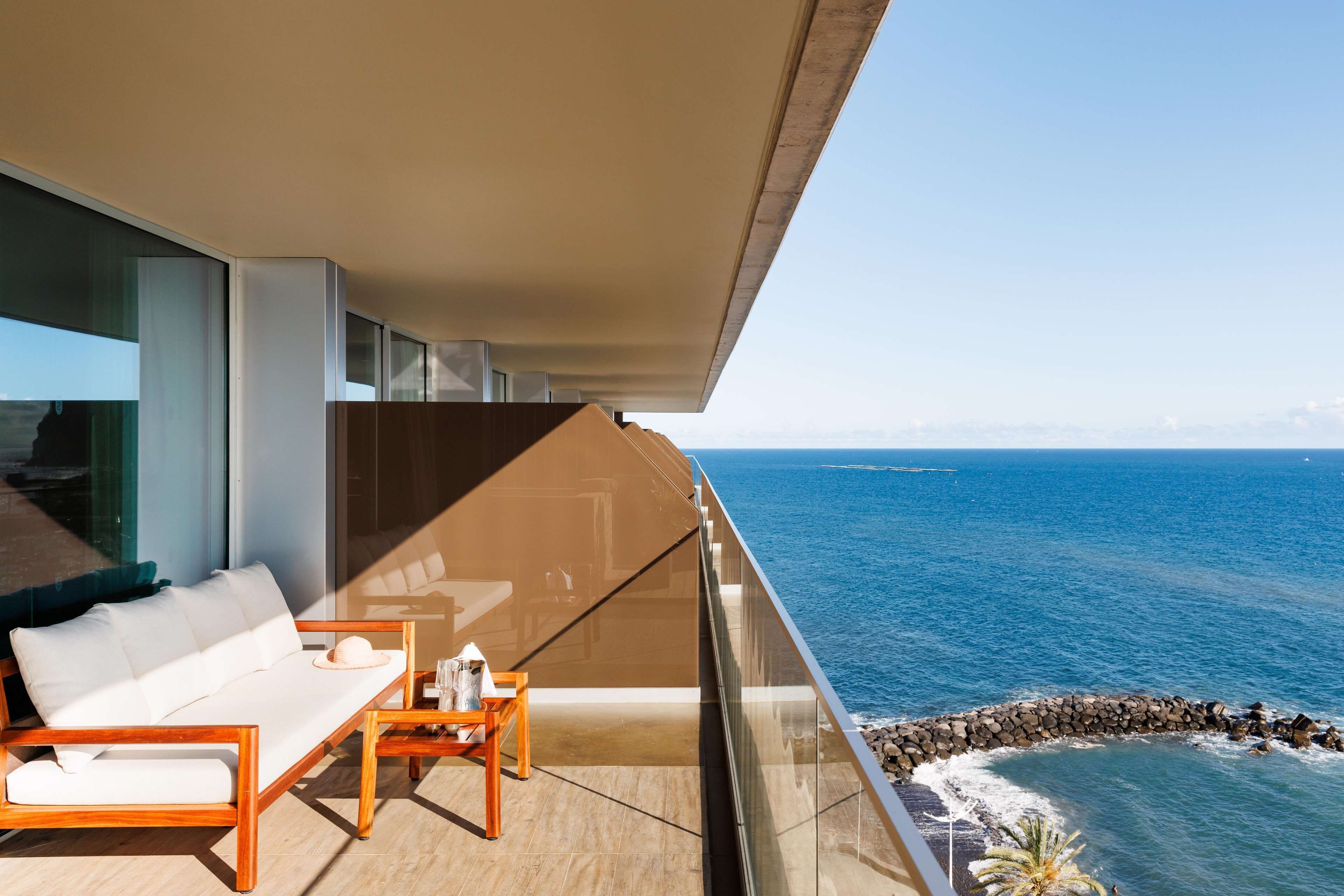 Un balcon avec un canapé blanc, une table en bois et une vue sur l’océan.