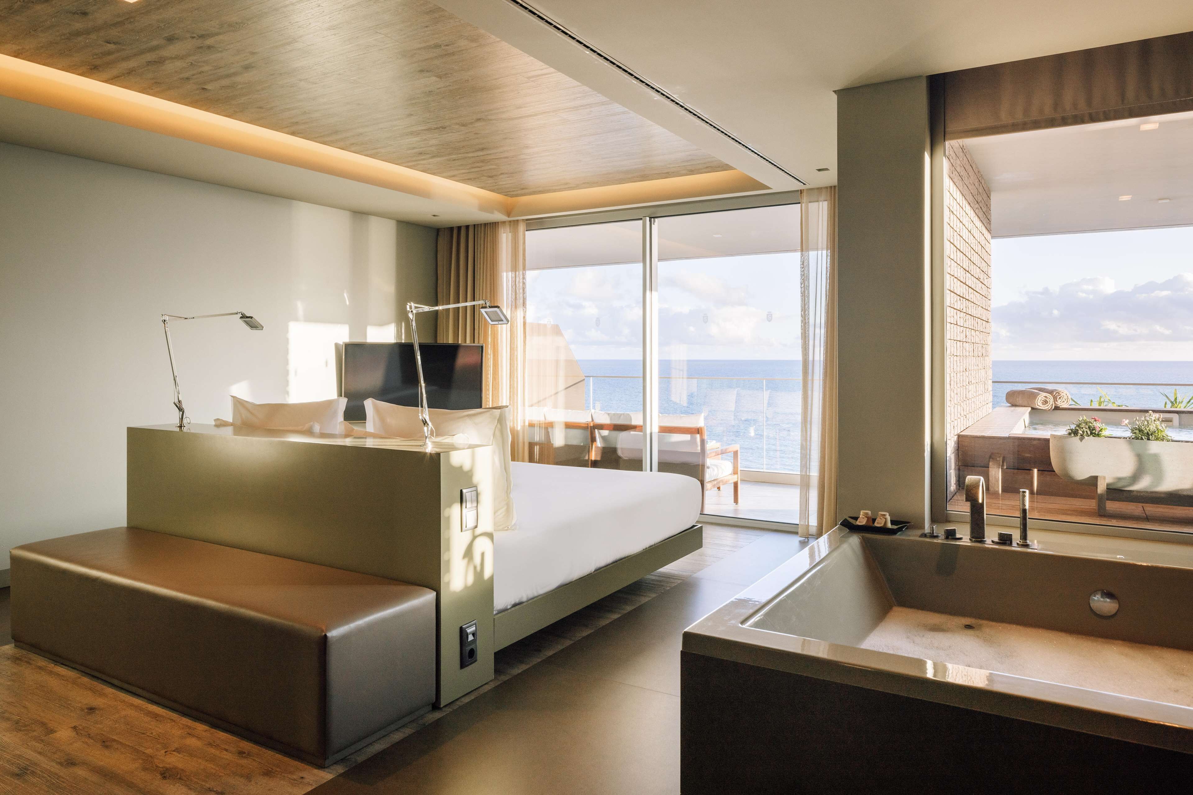 A modern hotel room with a large bed, a seating area, a desk, and a view of the ocean.