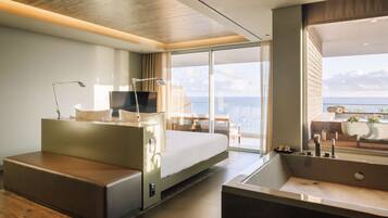 Une chambre d’hôtel moderne dotée d’un grand lit, d’un coin salon, d’un bureau et offrant une vue sur l’océan.