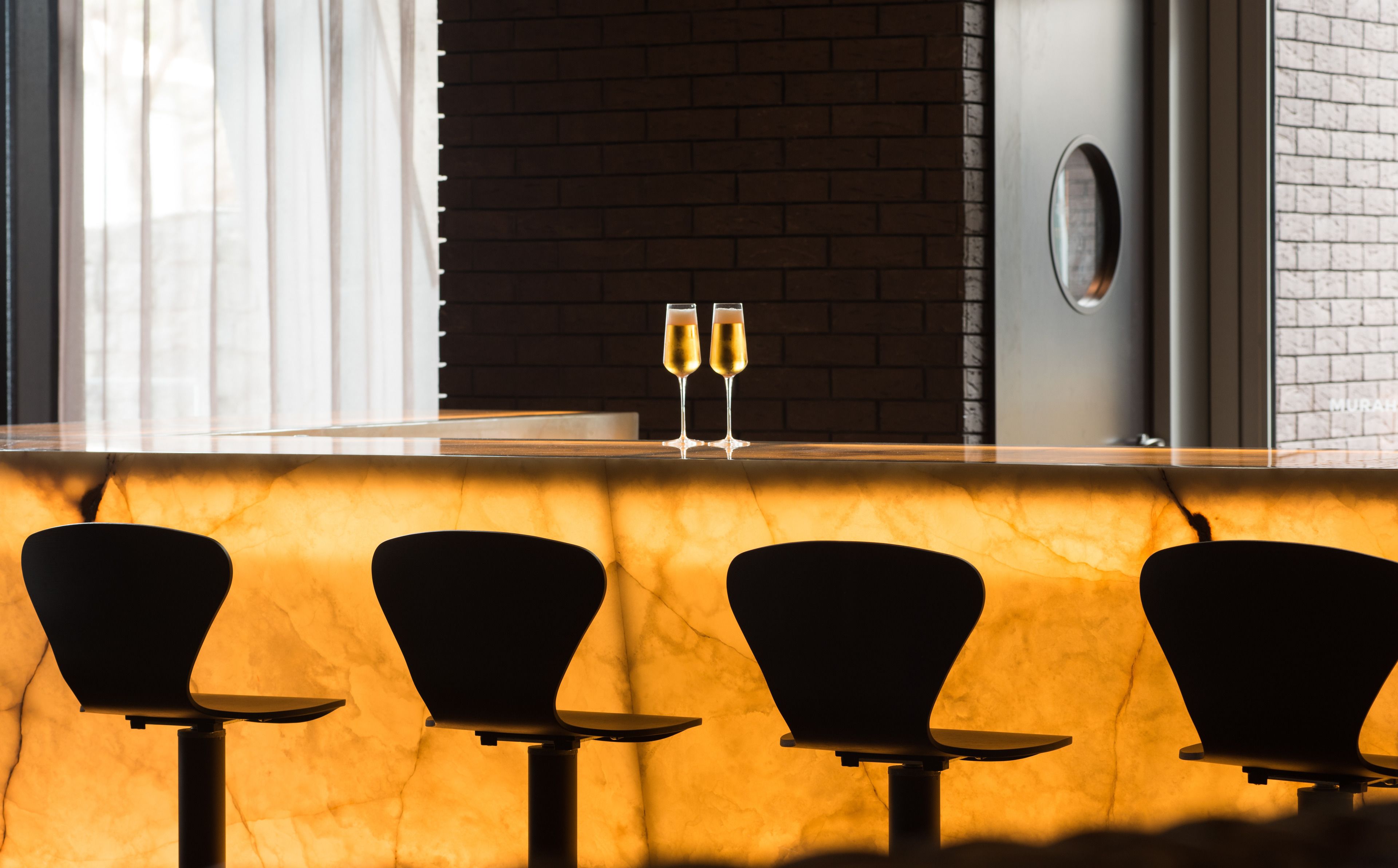 A bar area with a marble countertop, two glasses of champagne, and three black chairs.