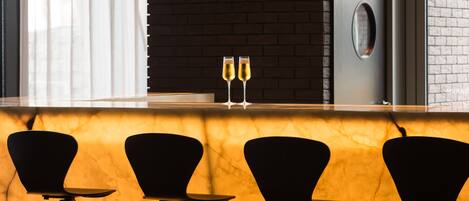 A bar area with a marble countertop, two glasses of champagne, and three black chairs.