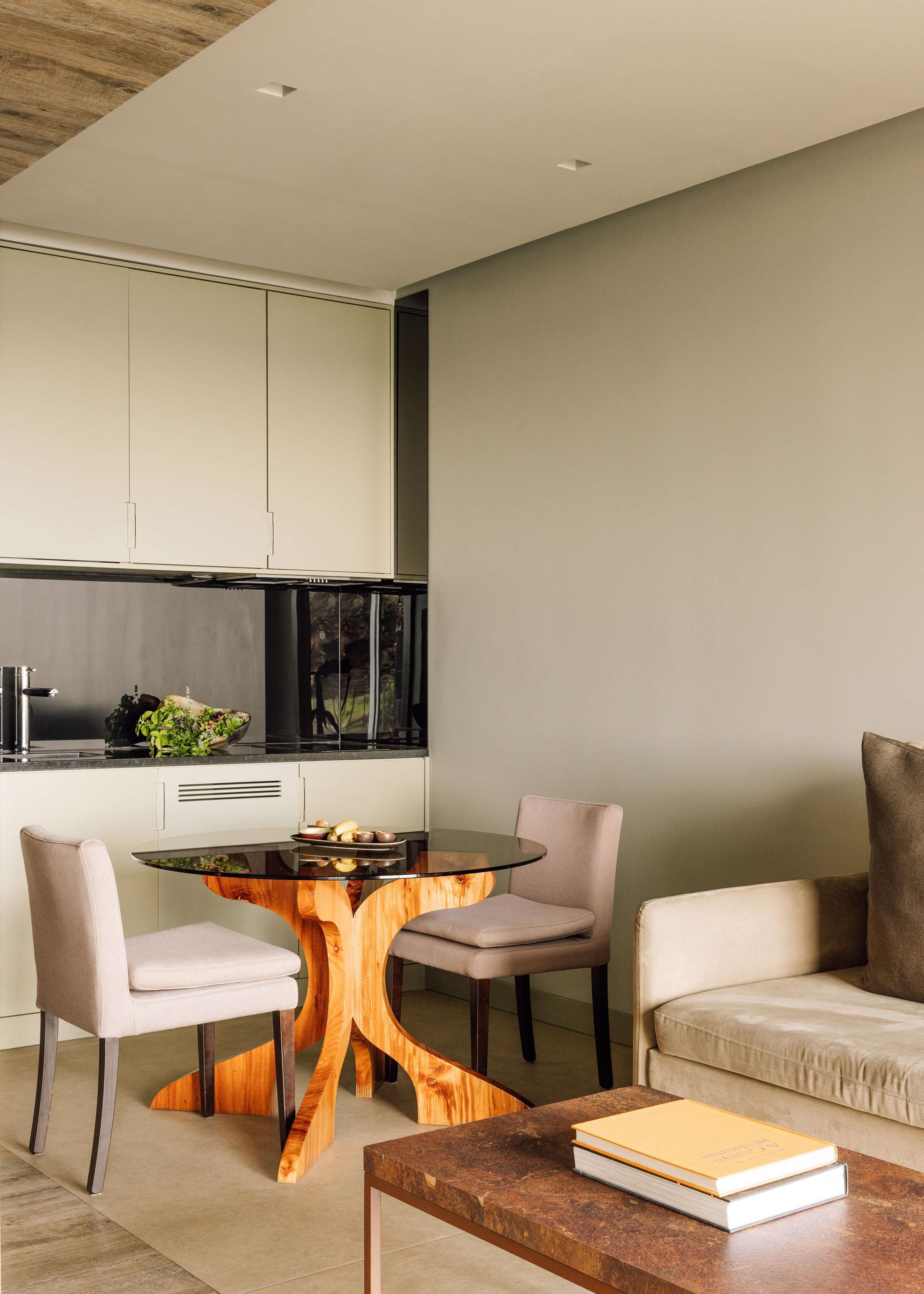 A modern kitchen with white cabinets, a black countertop, and a window. There is a dining table with chairs and a book on a side table.