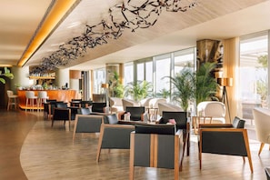 A modern hotel lobby with a curved seating area, a reception desk, and large windows offering views of the outdoors.