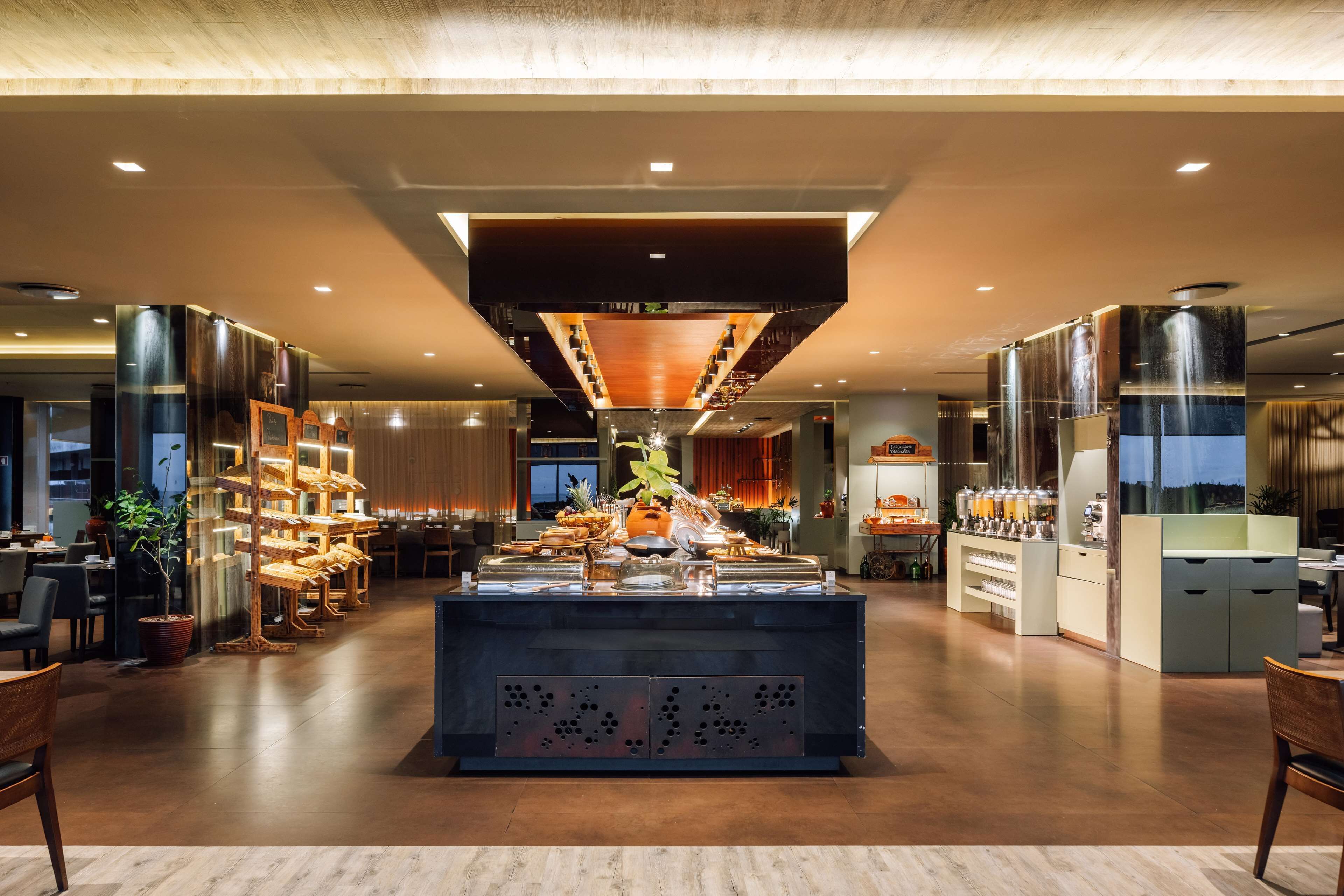 A modern hotel lobby with a central buffet, seating areas, and a staircase leading to upper floors.