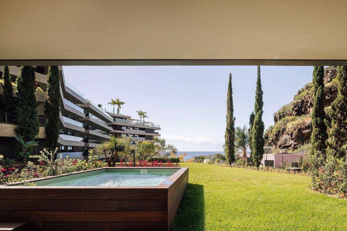 A modern hotel with a swimming pool, lush greenery, and a view of the ocean.