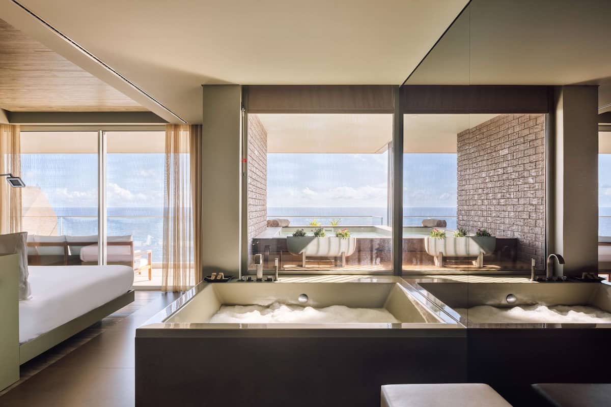 A modern bathroom with two large tubs and a view of the sea.