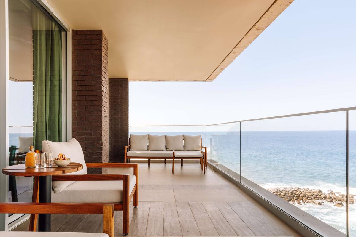 A balcony with a wooden table, two sofas, and a view of the ocean.