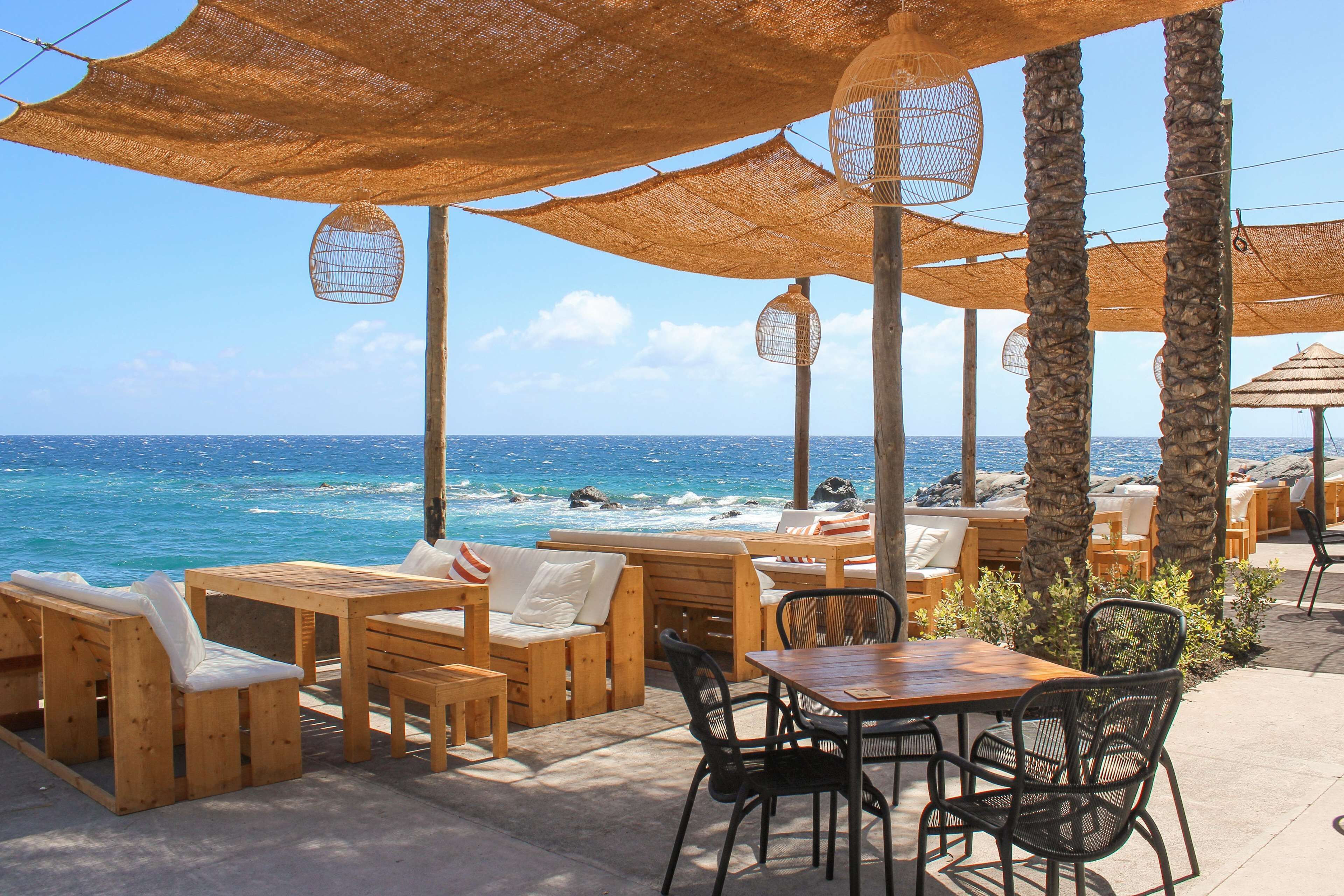 An outdoor seating area with wooden furniture and thatched umbrellas overlooking the ocean.