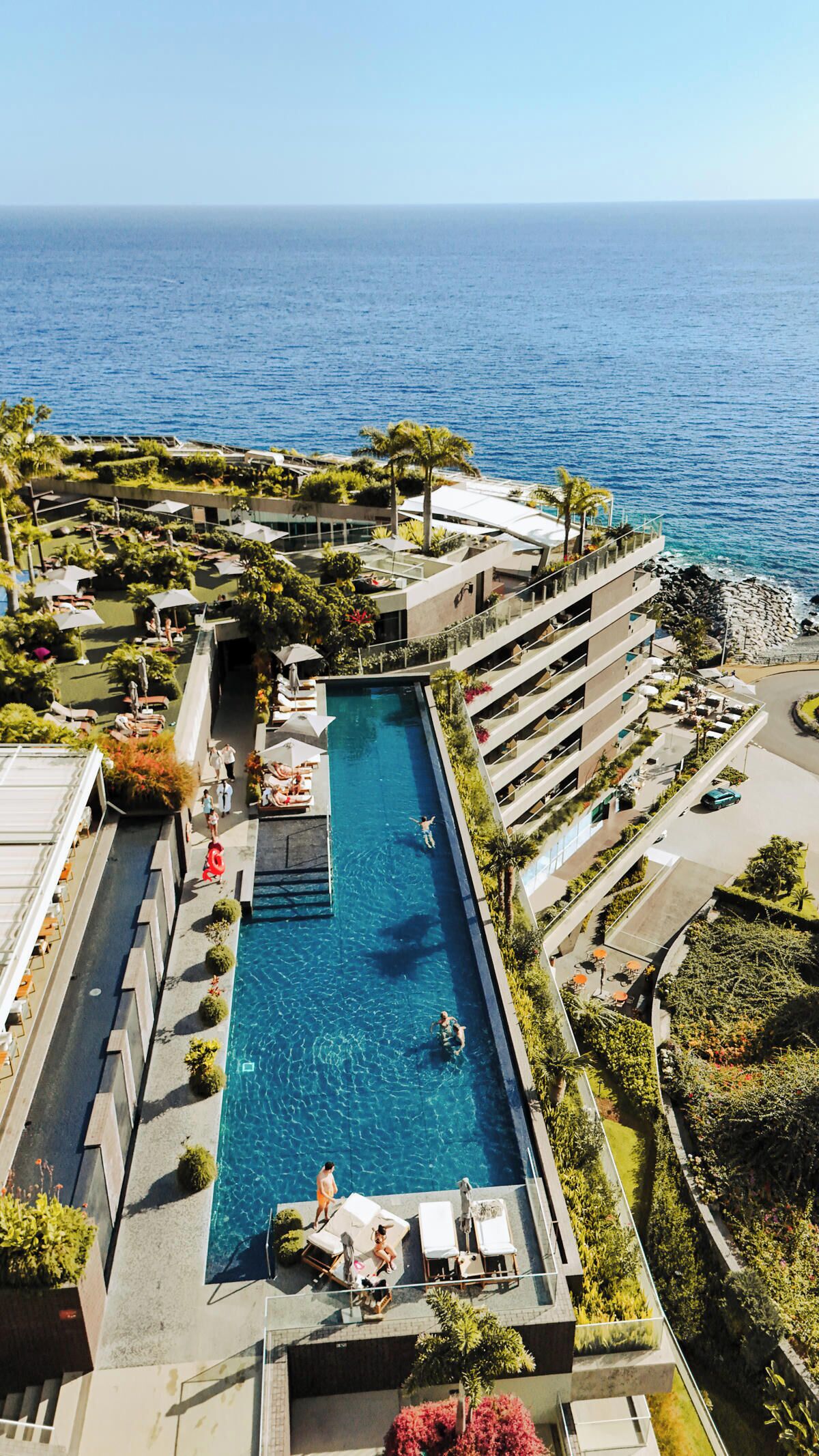 Un hotel con piscina centrale, area salotto esterna e vista sull'oceano.