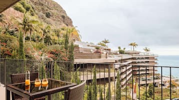 A balcony with wicker furniture, a glass table, and two glasses of orange juice.